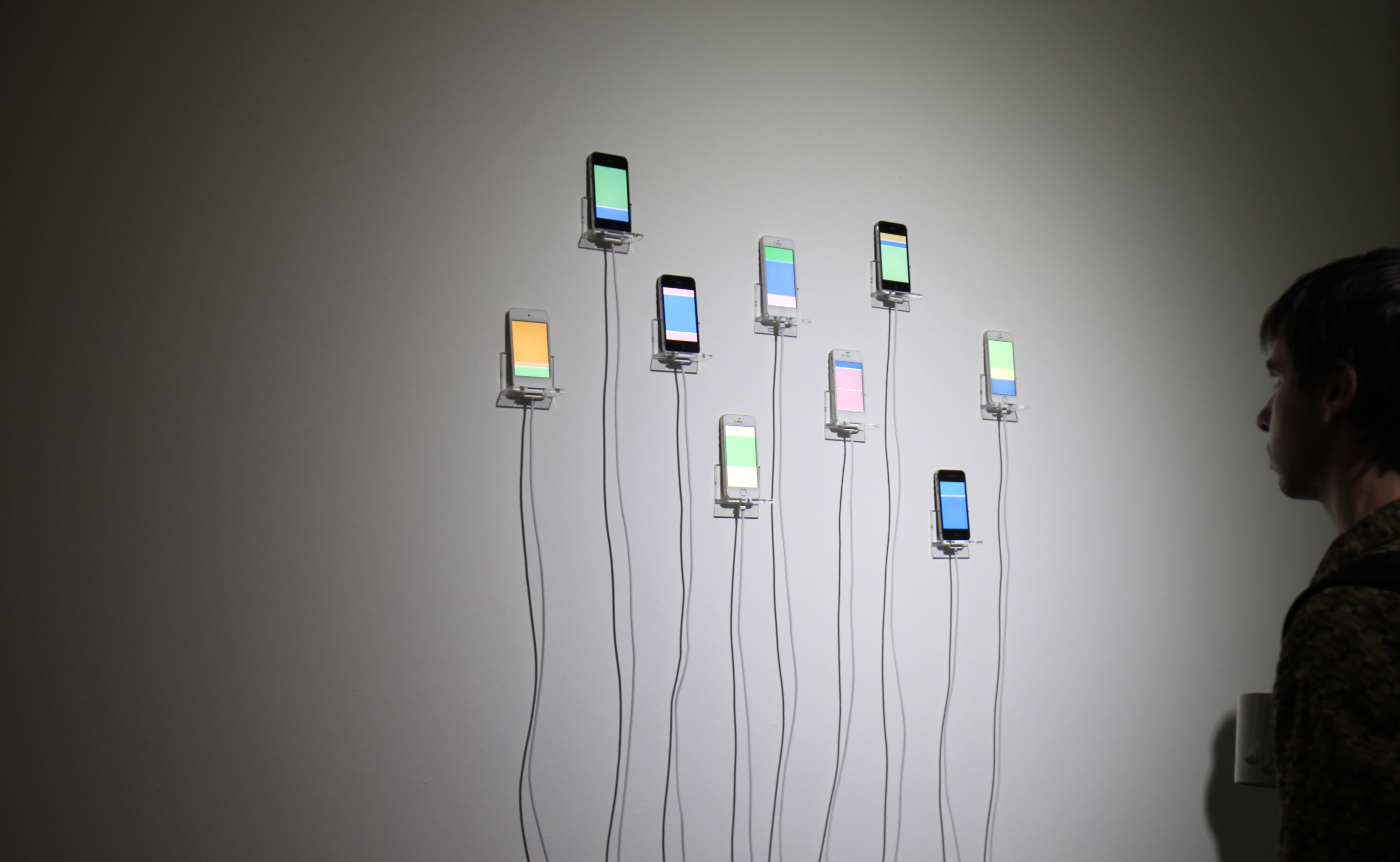 Man observes the iPhones in Infinite Scroll mounted on the wall, each scrolling bright colors